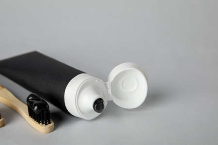 Tube with black tooth paste and bamboo brush on gray background