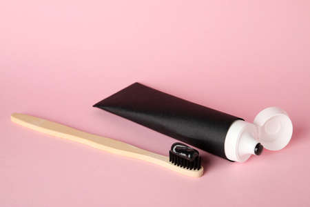 Tube of black tooth paste with brush on pink background