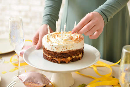 Woman decorating tasty birthday cake with candles at table