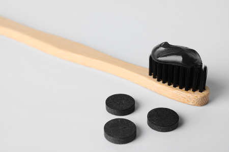 Bamboo brush with black toothpaste and activated carbon pills on white background
