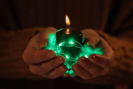 Woman holding burning candle with glowing green lights, closeup