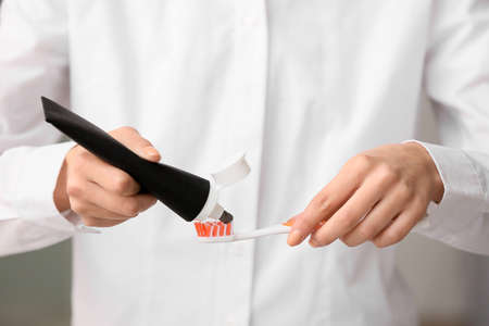 Woman applying black tooth paste onto plastic brush, closeup