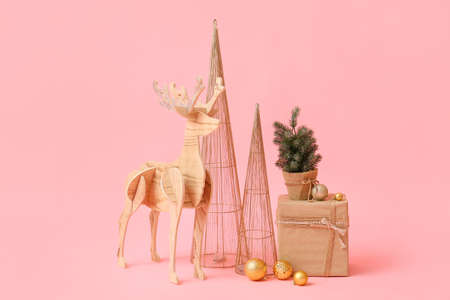 Wooden reindeer with small Christmas tree, present and decor on pink backgroundの写真素材