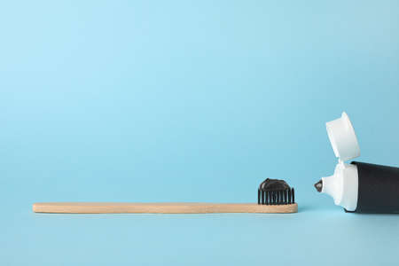 Bamboo brush with black tooth paste and tube on blue background