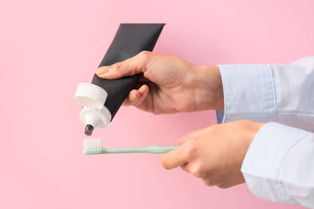 Woman applying black tooth paste onto plastic brush on pink background, closeupの写真素材