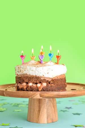 Wooden stand with tasty birthday cake and confetti on green background
