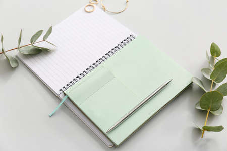 Stylish notebooks with eucalyptus and jewelry on light background