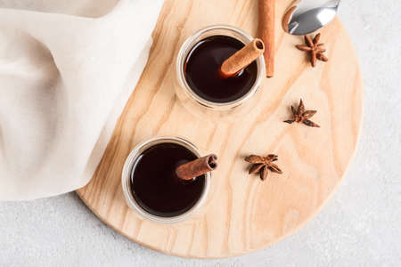 Glasses of tasty coffee with cinnamon on light background