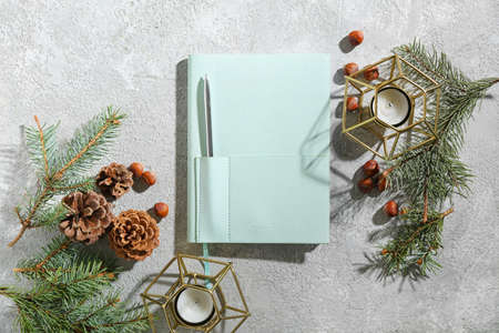 Stylish notebook with fir branches, cones, hazelnuts and candles on grunge backgroundの写真素材
