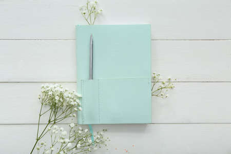 Stylish notebook with pen and gypsophila flowers on white wooden background