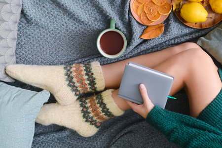 Woman with notebook, cup of tea, food and autumn leaves on gray plaidの写真素材