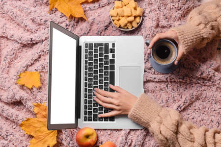 Woman with cup of coffee using laptop on pink fabric backgroundの写真素材