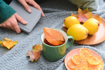 Green cup of hot tea, food and fallen leaves on gray fabric background, closeupの写真素材