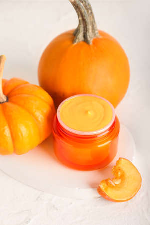 Jar of natural mask and ripe pumpkins on light background, closeup