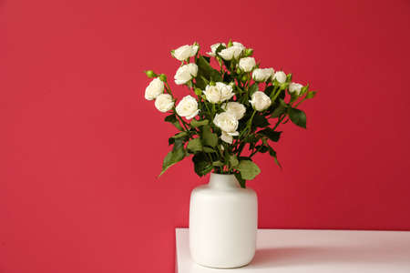 Vase with bouquet of beautiful roses on table near red wallの写真素材