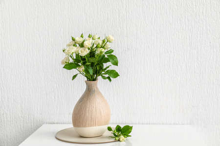 Vase with bouquet of beautiful roses on table near white wallの写真素材