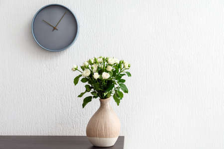 Vase with bouquet of beautiful roses on table near white wallの写真素材
