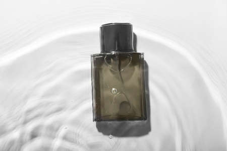 Bottle of perfume for men in water on light background