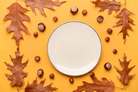 Composition with table setting, chestnuts and autumn leaves on yellow backgroundの写真素材