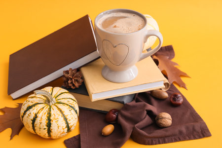 Cup of tasty pumpkin coffee and books on yellow backgroundの写真素材