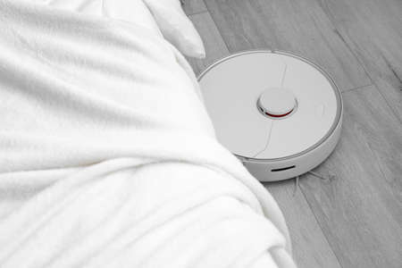 Modern robot vacuum cleaner on wooden floor in bedroom