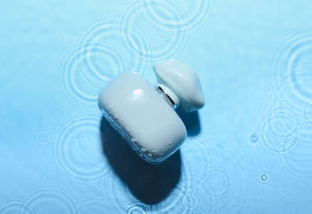 Bottle of perfume in water on blue background