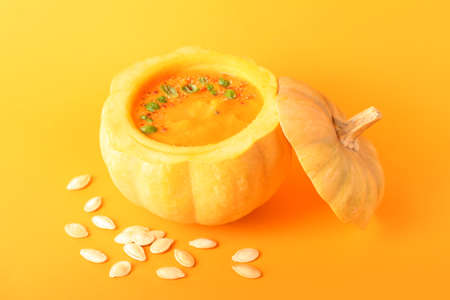 Tasty cream soup served in pumpkin and seeds on color backgroundの写真素材