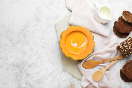 Tasty soup served in pumpkin with bread on light backgroundの写真素材