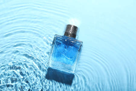 Bottle of perfume in water on blue background