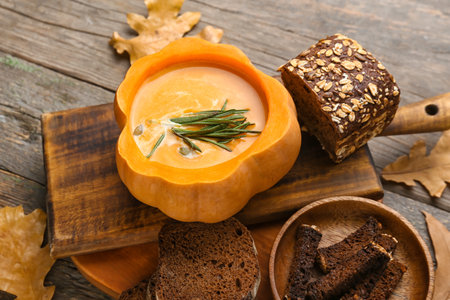 Tasty soup served in pumpkin with bread on wooden backgroundの写真素材