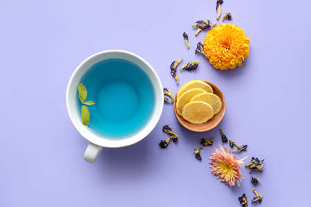 Composition with cup of blue tea, lemon and dried butterfly pea flowers on color backgroundの写真素材