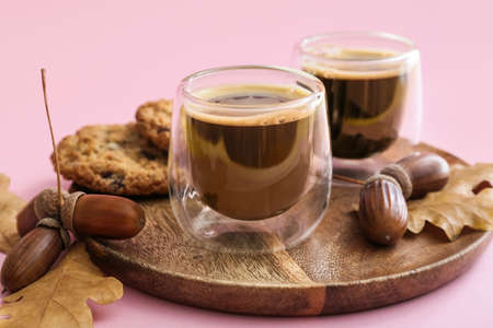 Glass cups of coffee with acorns, autumn leaves and cookies on pink backgroundの写真素材