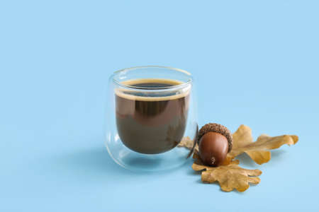 Glass cup of coffee with acorn and autumn leaves on blue background