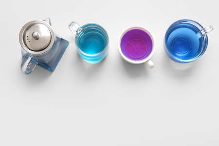 Teapot and cups of blue tea on light background