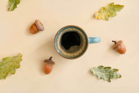 Cup of coffee with acorns and autumn leaves on beige backgroundの写真素材