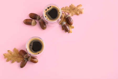 Glass cups of coffee with acorns and autumn leaves on pink background