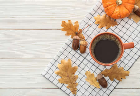 Cup of coffee with acorns, autumn leaves and pumpkin on light wooden background