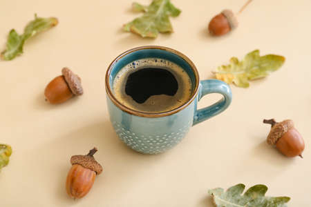 Cup of coffee with acorns and autumn leaves on beige backgroundの写真素材