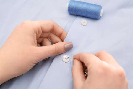 Woman sewing button on shirt, closeupの写真素材