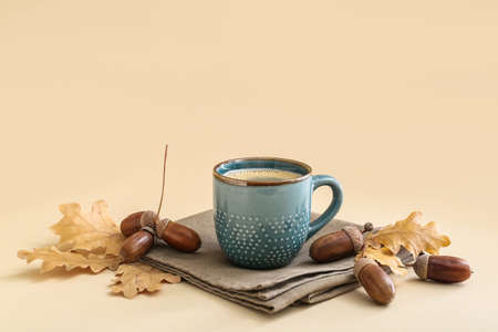 Cup of coffee with acorns and autumn leaves on beige backgroundの写真素材