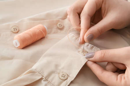 Woman sewing button on shirt sleeve, closeupの写真素材
