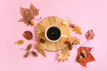 Composition with cup of coffee, acorns and autumn leaves on pink background