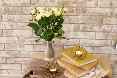 Vase with bouquet of beautiful fresh roses on table near beige brick wallの写真素材