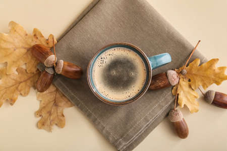 Cup of coffee with acorns and autumn leaves on beige background