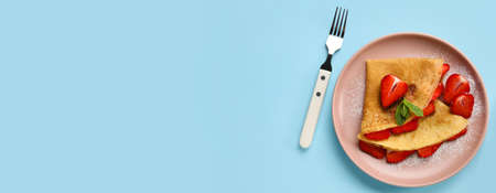 Plate of thin pancakes with strawberry and fork on blue background with space for textの写真素材