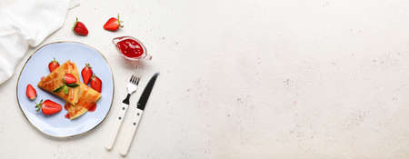 Plate of thin pancakes with strawberries, jam and cutlery on light background with space for textの写真素材