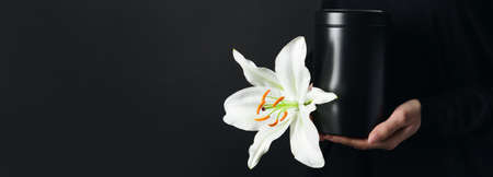 Woman holding mortuary urn and lily flower on black background with space for text, closeupの写真素材