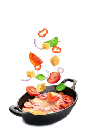 Baking dish with tasty Shakshouka and flying fresh ingredients on white backgroundの写真素材