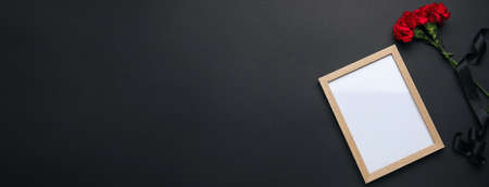 Black funeral ribbon, blank photo frame and carnation flowers on dark background with space for textの写真素材