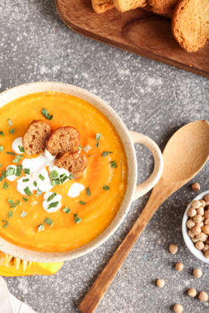 Pot with delicious pumpkin cream soup on gray background
